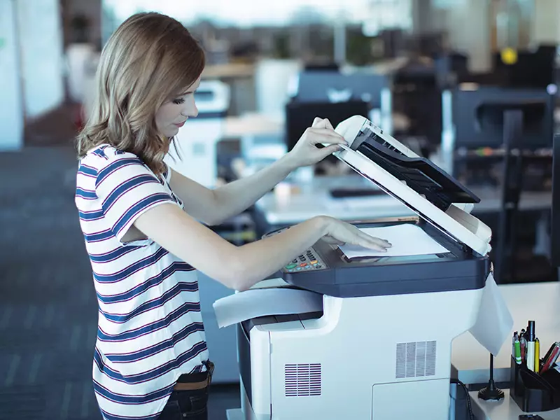 Nainen asettaa paperia kopiokoneeseen toimistossa.