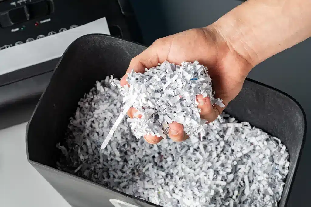 Lähikuvassa miehen käsi pitää silputtua paperia.